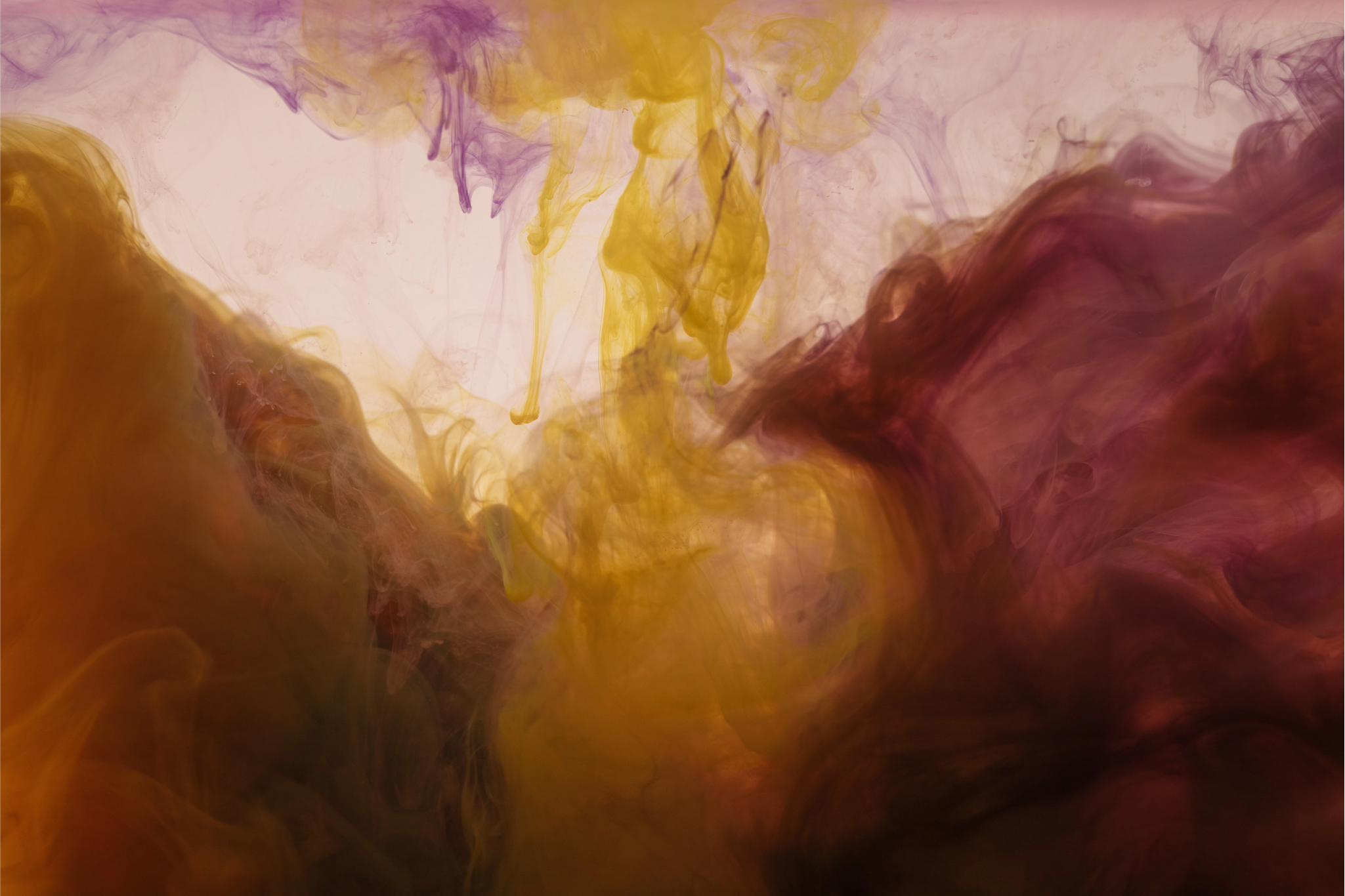 Das Bild zeigt eine faszinierende Darstellung von sich mischenden Farben in einer Flüssigkeit, welche eine Art abstrakte Kunst bildet. Man sieht einen Wirbel von intensiven und lebhaften Farben – darunter Töne von Gelb, Lila und Dunkelrot –, die sich in einer unbekannten Flüssigkeit ausbreiten und vermischen. Die Farben fließen in eleganten, rauchartigen Mustern, was eine organische und dynamische Bewegung suggeriert. Die unterschiedliche Dichte und Transparenz der Farben schaffen eine Tiefenillusion, wodurch das Bild eine fast dreidimensionale Qualität erhält. Dieser Effekt erzeugt eine ästhetische und visuell ansprechende Komposition, die die Betrachter zur Interpretation und zum Nachdenken anregt.